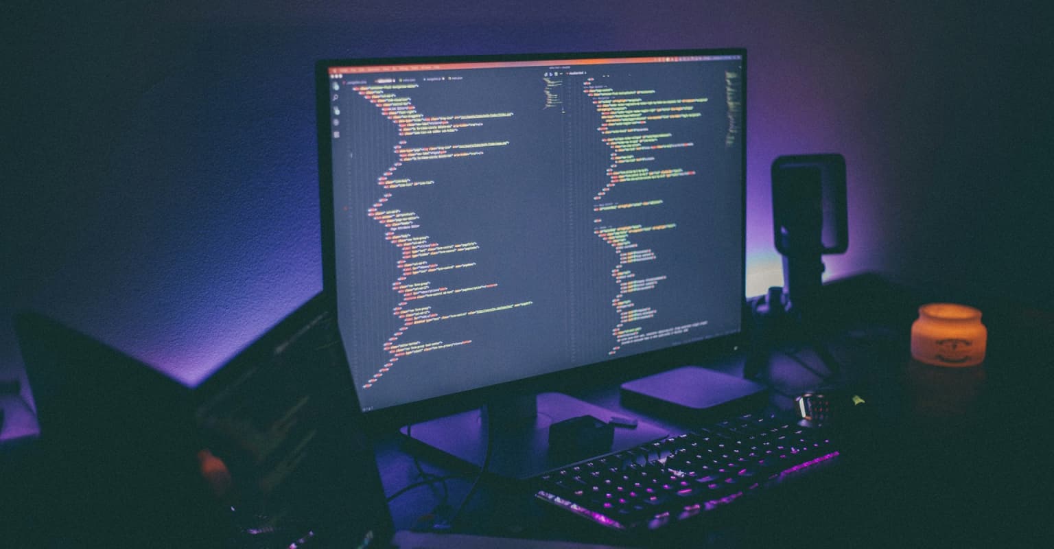 desk setup with monitor and code on screen and ambient purple lighting